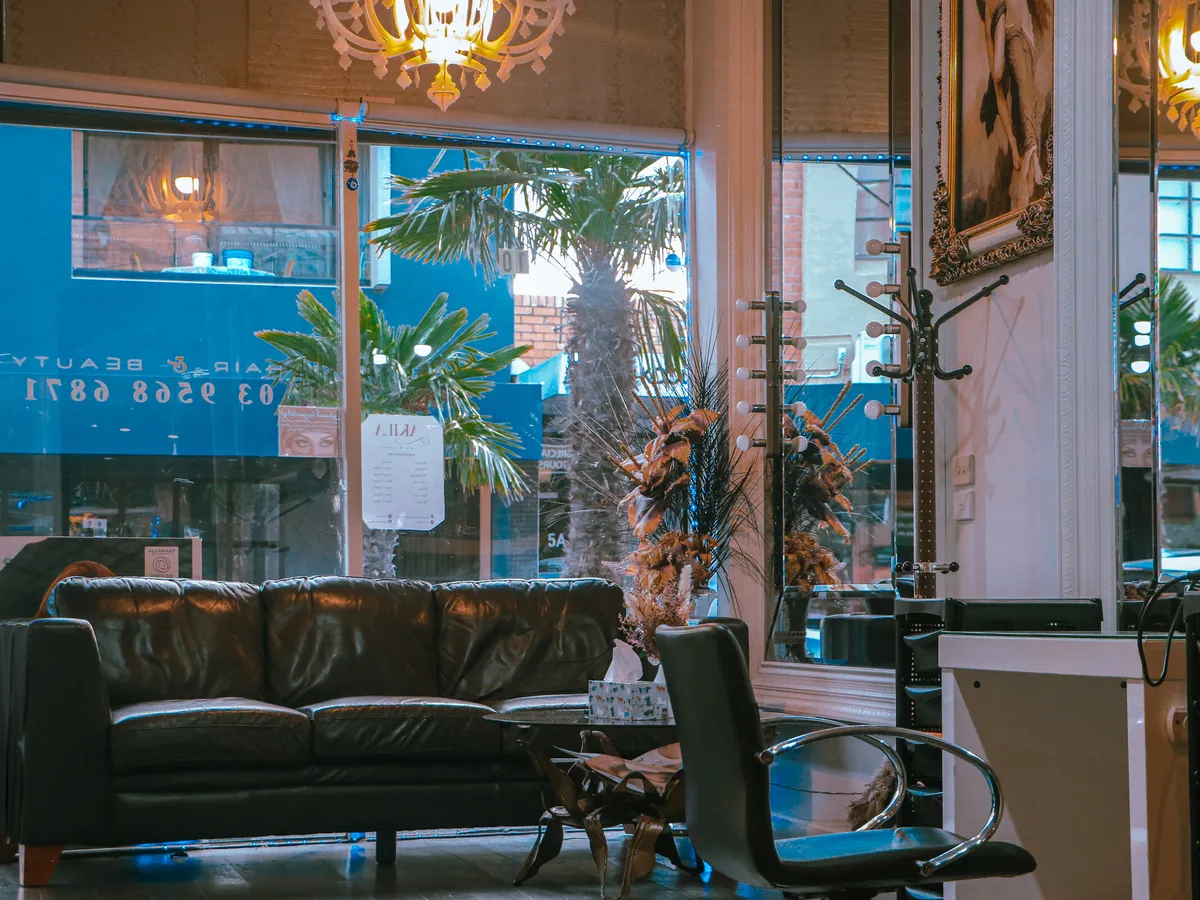 The front of the salon at Akila, Station Street, Oakleigh: the leather sofa by the window, palms outside and the chandelier above