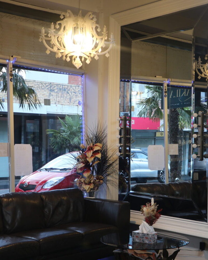 Akila's waiting area on Station Street, Oakleigh: chandelier, large mirror, leather couch, and the shopfront window onto the street